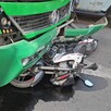 Camión verde de la ruta 360 en Guadalajara con la fascia rota y una motocicleta debajo tumbada en el pavimento mojado