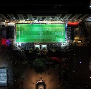Vista aérea nocturna de una cancha de fútbol rápido iluminada en una plaza pública de Guadalajara, rodeada de edificios y personas observando.