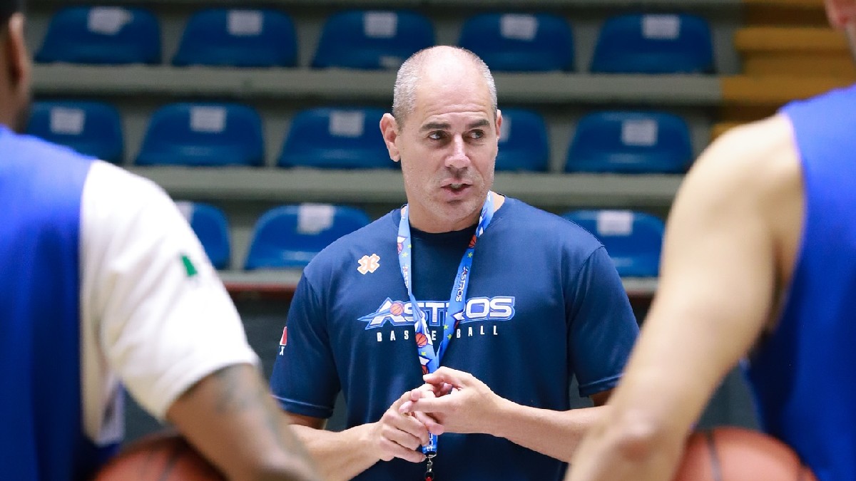 Un hombre con ropa deportiva azul posa con los brazos cruzados frente a las gradas de un estadio, vistiendo una camiseta de los Astros de Jalisco.