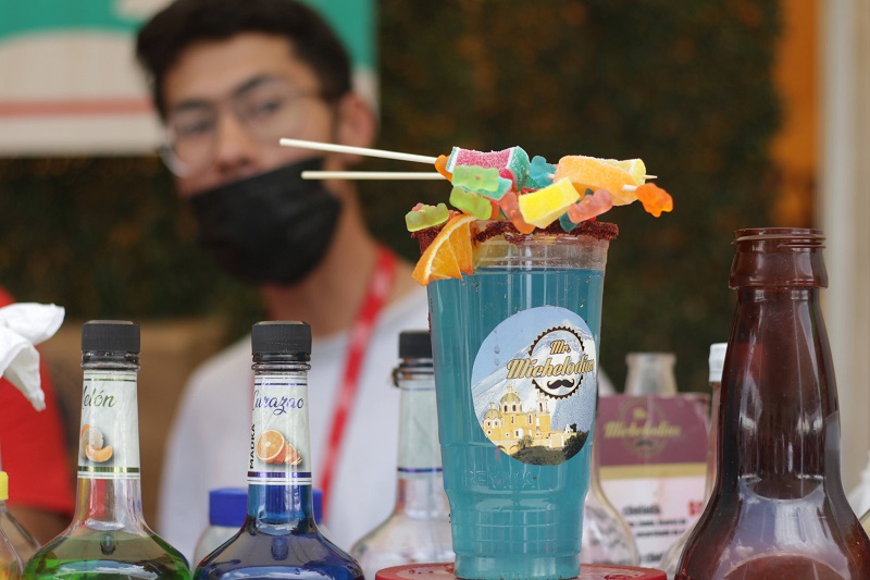 Una michelada servida en un vaso de plástico, acompañado de gomitas.