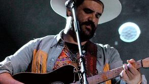 Hombre de barba y sombrero tocando la guitarra acústica.