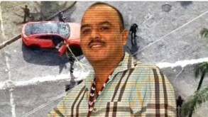 Un retrato en primer plano de un hombre sonriente con camisa de cuadros, superpuesto sobre una escena difusa de un vehículo rojo en una calle.