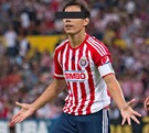 Un jugador de las Chivas con uniforme rojiblanco y gafete de capitán abre los brazos en el campo; sus ojos están cubiertos por una barra negra.