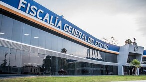 Fachada moderna y acristalada del edificio de la Fiscalía General del Estado, con un letrero azul de grandes letras blancas en la parte superior.