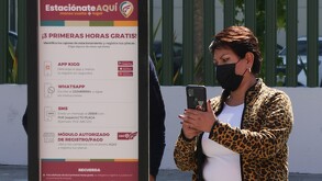 Mujer con celular en la mano frente a un anuncio de parquímetros en Puebla.
