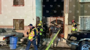 Se observan unas viviendas, y unas personas afuera, hay una cinta amarilla de precaución.