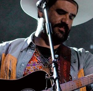 Hombre de barba y sombrero tocando la guitarra acústica.