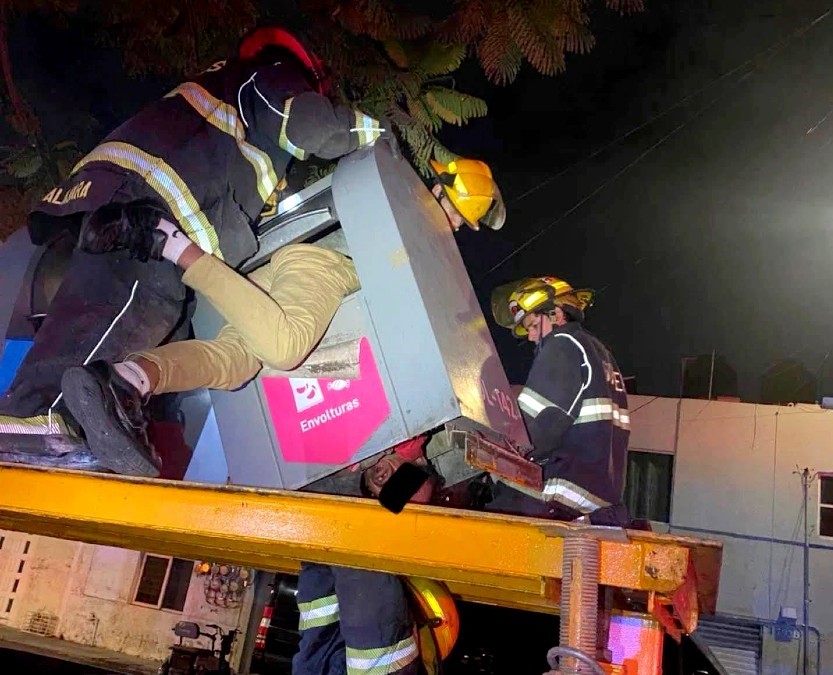 Bomberos de Guadalajara maniobrando un contenedor de basura para sacar a un hombre con las piernas de fuera