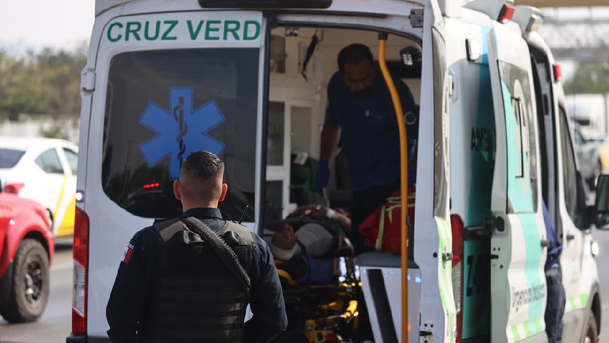 Oficial de la Policía de Zapopan visto de espaldas detrás de una ambulancia de la Cruz Verde con un paramédico y una mujer dentro