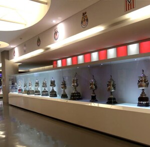 Una hilera de trofeos de fútbol plateados se exhibe dentro de vitrinas iluminadas en el museo oficial de las Chivas del Guadalajara bajo luces LED.