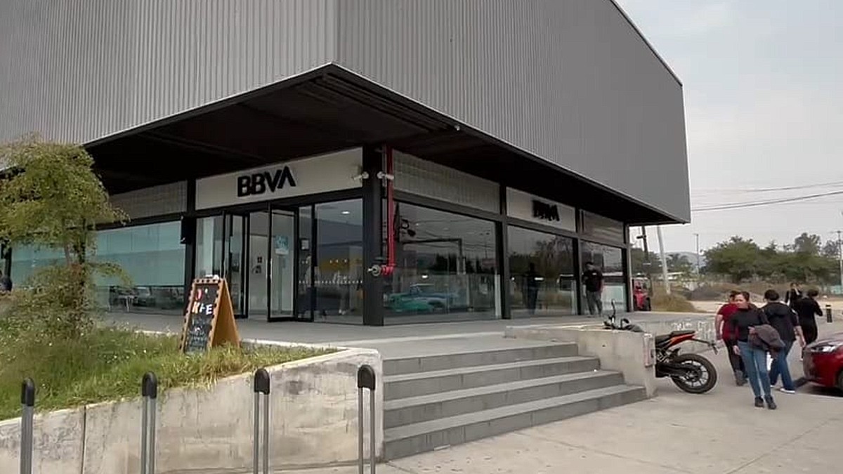 Vista del exterior de una sucursal del banco BBVA con personas y autos estacionados alrededor