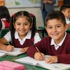Niños de primaria en un salón de clases sonriendo a la cámara. Beca Rita Cetina.