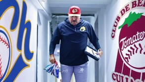 El mánager de los Charros de Jalisco camina por un pasillo del estadio sosteniendo bolsas de botanas, entre los logos de Charros y Tomateros.