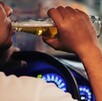 Se ve a un hombre tomando un líquido de una botella y él viste una playera blanca; está dentro de un auto.