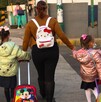 Se observa a una mujer que lleva de la mano a dos niñas que traen mochilas.