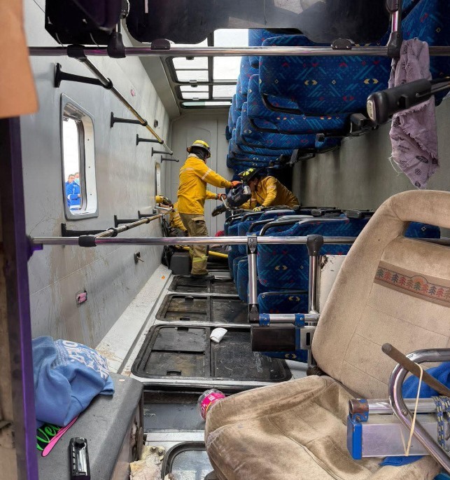 Elementos de Protección Civil dentro de un camión volcado sobre su costado con asientos y objetos dañados alrededor