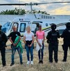 Tres personas detenidas con rostros pixelados aparecen frente a un helicóptero ambulancia, custodiadas por agentes de la SSPC y la Guardia Civil.
