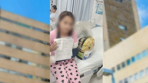 Una niña sentada en una cama de hospital con el brazo vendado sostiene documentos oficiales; a los costados se ven tomas borrosas de un edificio.