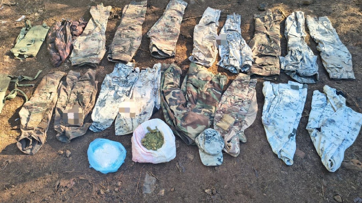 Dos soldados del Ejército Mexicano, de espaldas y con equipo táctico, vigilan un campamento improvisado con lonas negras en una zona boscosa.