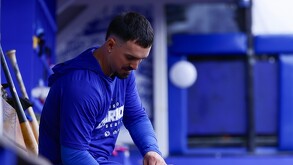 Un jugador de los Charros de Jalisco con sudadera azul de entrenamiento permanece sentado en el dugout, con varios bates de madera al lado.