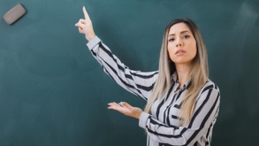 Maestra dando clases con ayuda de un pizarrón verde.