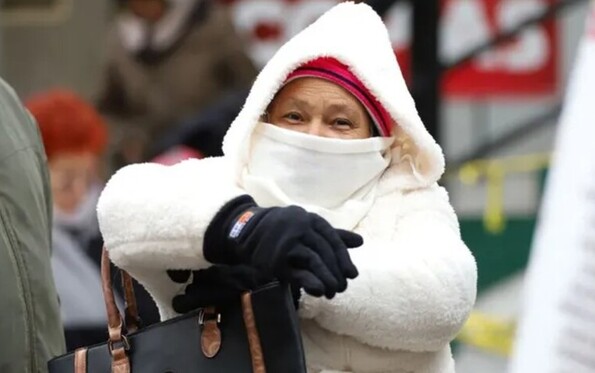 Adultos mayores cubiertos de los ojos hacia abajo y vistiendo abrigos, gorra y guantes con personas desenfocadas en el fondo