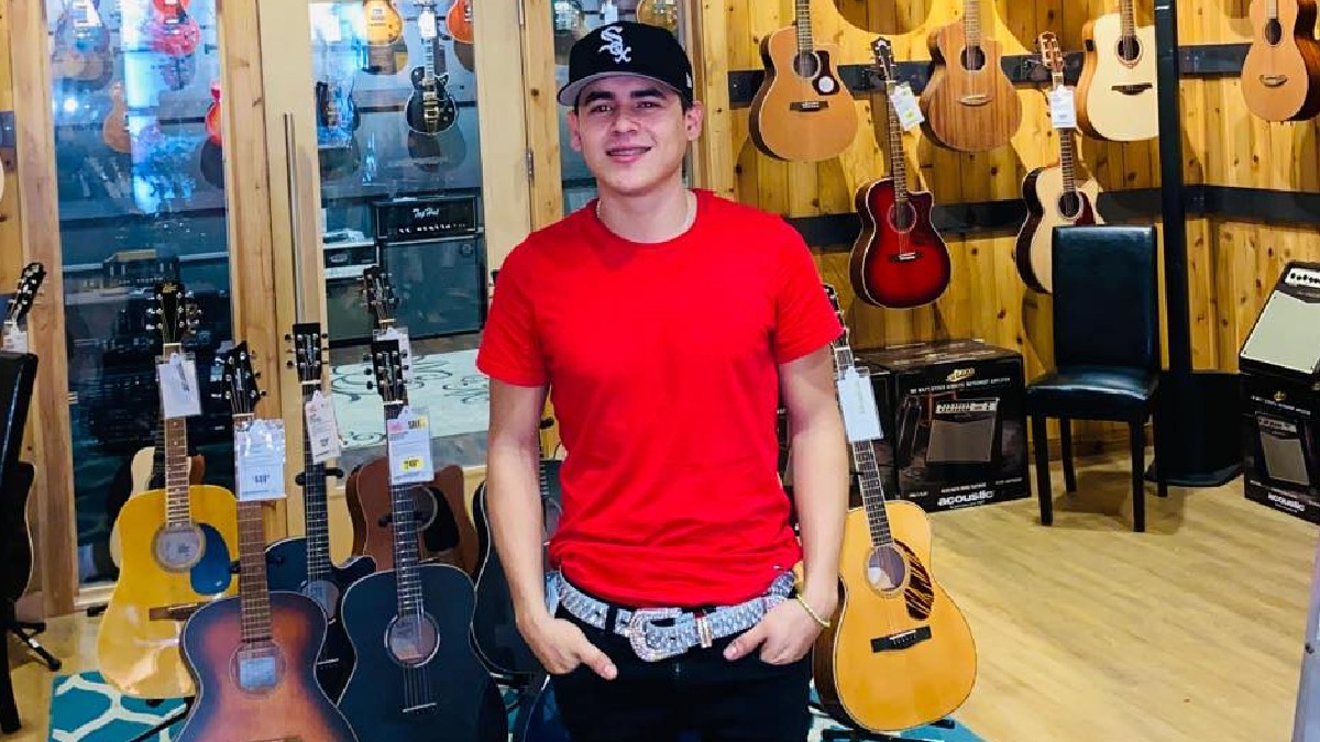 Joven con plaayera roja y gorra delante de varias guitarras