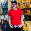 Joven con plaayera roja y gorra delante de varias guitarras