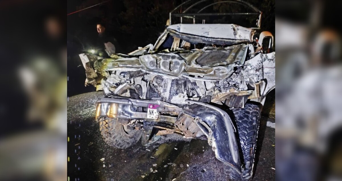 Vista frontal de una camioneta completamente destruida del frente tras un choque con una persona sosteniendo una linterna de fondo