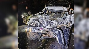 Vista frontal de una camioneta completamente destruida del frente tras un choque con una persona sosteniendo una linterna de fondo