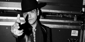 El cantante Christian Nodal, en una foto a blanco y negro, viste sombrero y chaleco de cuero mientras apunta con el dedo hacia la cámara.