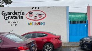 Se ve una fachada color blanca con puerta azul y letras que dicen Guardería Gratuita Los Pinos.