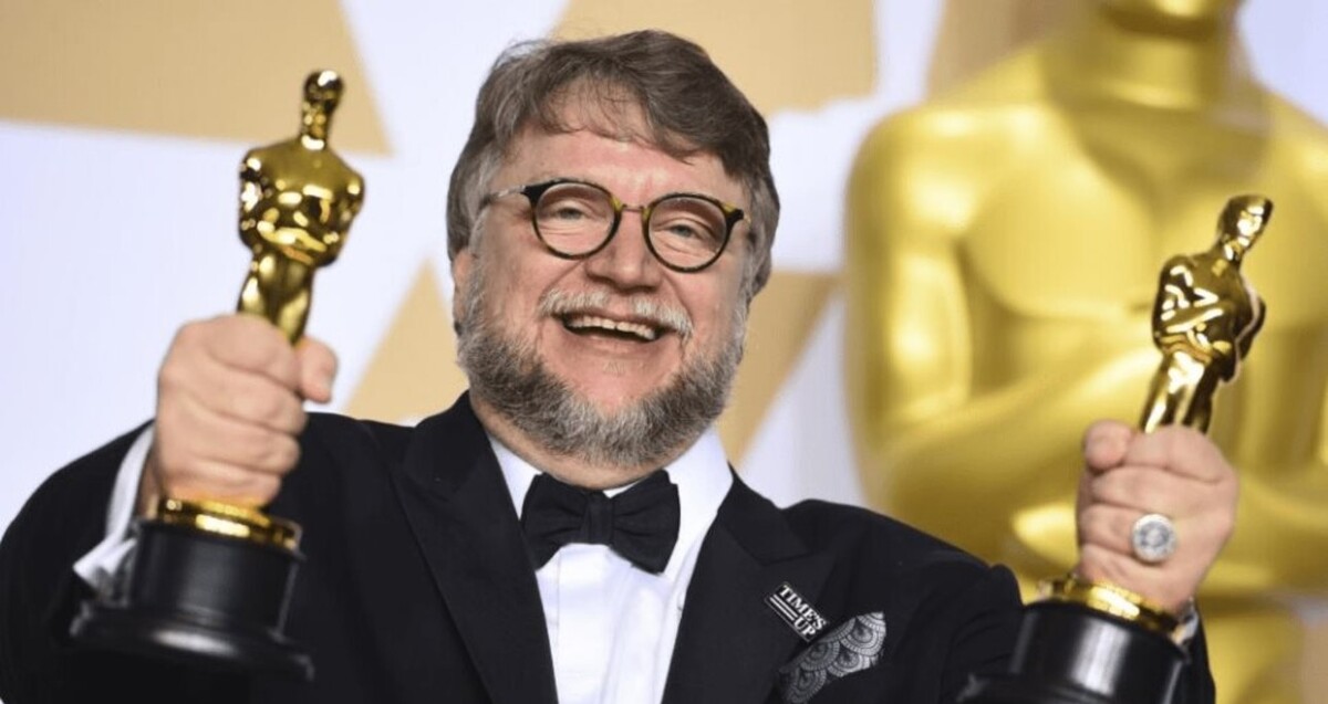 Guillermo del Toro vestido de traje sosteniendo dos estatuillas de los premios Oscar mientras sonríe