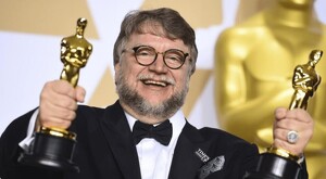 Guillermo del Toro vestido de traje sosteniendo dos estatuillas de los premios Oscar mientras sonríe