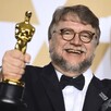 Guillermo del Toro vestido de traje sosteniendo dos estatuillas de los premios Oscar mientras sonríe