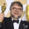 Guillermo del Toro vestido de traje sosteniendo dos estatuillas de los premios Oscar mientras sonríe