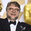 Guillermo del Toro vestido de traje sosteniendo dos estatuillas de los premios Oscar mientras sonríe