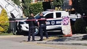 Policías junto a una patrulla municipal resguardan una zona de crimen.