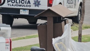 Bote de basura al costado de una banqueta con bolsas alrededor y una patrulla de la Policía de Tlajomulco de fondo