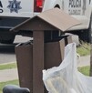 Bote de basura al costado de una banqueta con bolsas alrededor y una patrulla de la Policía de Tlajomulco de fondo