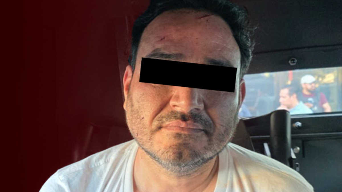 Hombre identificado como César N alias El Botox viendo de frente con los ojos censurados por un recuadro negro con una pantalla de fondo