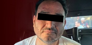 Hombre identificado como César N alias El Botox viendo de frente con los ojos censurados por un recuadro negro con una pantalla de fondo