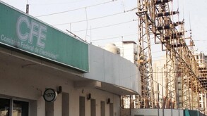 Vista de un edificio con cartel de la CFE con una subestación eléctrica y torres de electricidad detrás