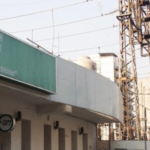 Vista de un edificio con cartel de la CFE con una subestación eléctrica y torres de electricidad detrás