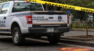 Parte de atrás de una patrulla de la Fiscalía del Estado de Michoacán estacionada al lado de un parque con una cinta policiaca amarilla en primer plano