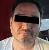 Hombre identificado como César N alias El Botox viendo de frente con los ojos censurados por un recuadro negro con una pantalla de fondo