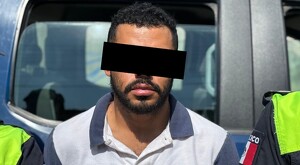 Hombre con barba y con los ojos censurados por un recuadro negro delante de una patrulla con dos policías a los lados