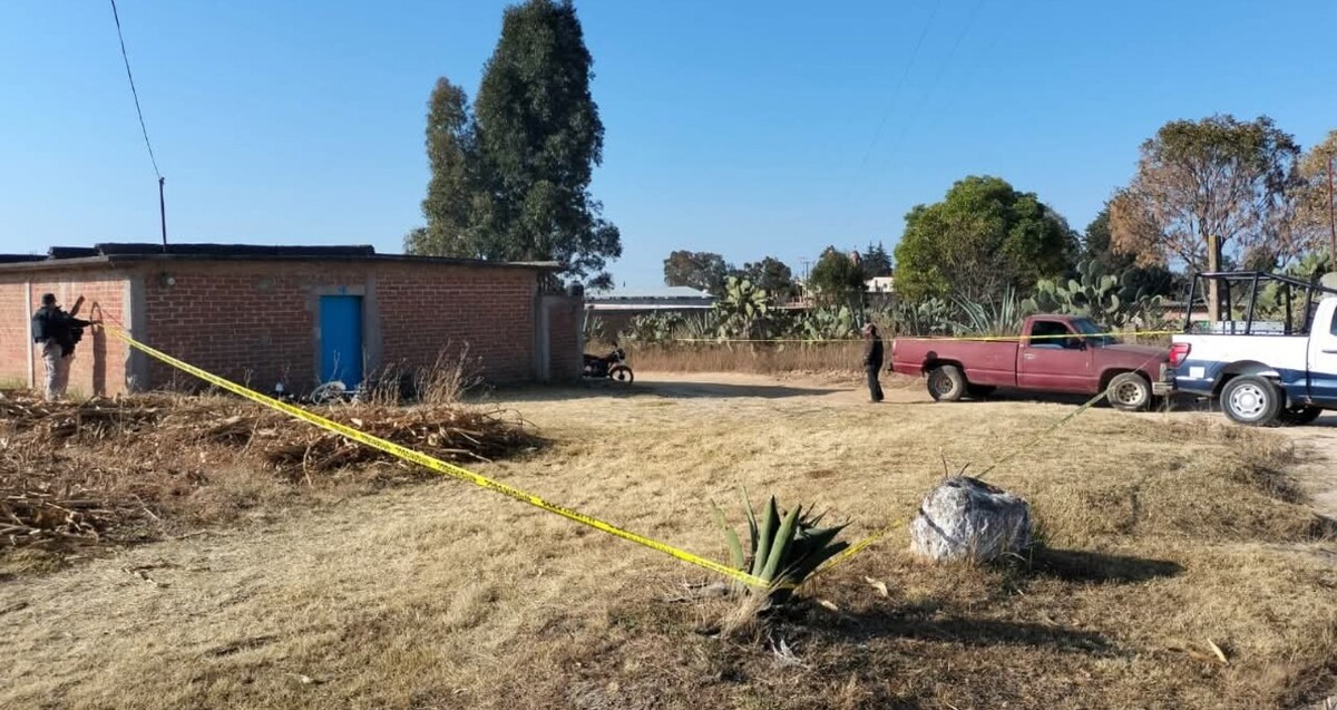 Terreno acordonado por una cinta policiaca con una camioneta roja, una patrulla de Michoacán, policías y una pequeña construcción dentro