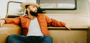 Se observa a un hombre con barba y sombrero sentado en una camioneta.