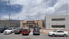 Se observa un edificio color beige y unos autos estacionados afuera.